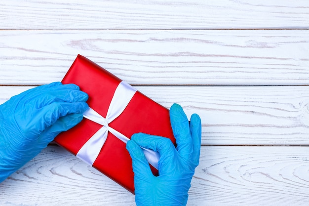 Manos enguantadas sostienen una caja de regalo roja con una cinta sobre un fondo de madera