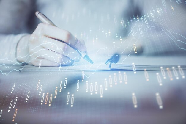 Manos escribiendo información sobre el mercado de valores en el bloc de notas gráficos de divisas hologramas en el frente concepto de investigación exposición múltiple