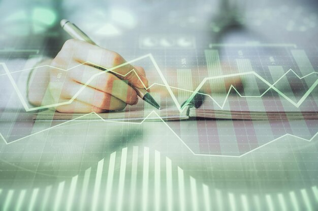 Manos escribiendo información sobre el mercado de valores en el bloc de notas gráficos de divisas hologramas en el frente concepto de investigación exposición múltiple