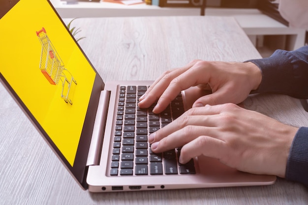 Manos escribiendo en el teclado de la computadora portátil con el carrito de compras en exhibición Imagen conceptual de las compras en línea Experiencia minorista digital moderna