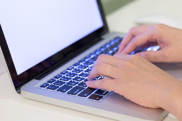 Foto manos escribiendo texto en un teclado de computadora portátil en la mesa de madera blanca.
