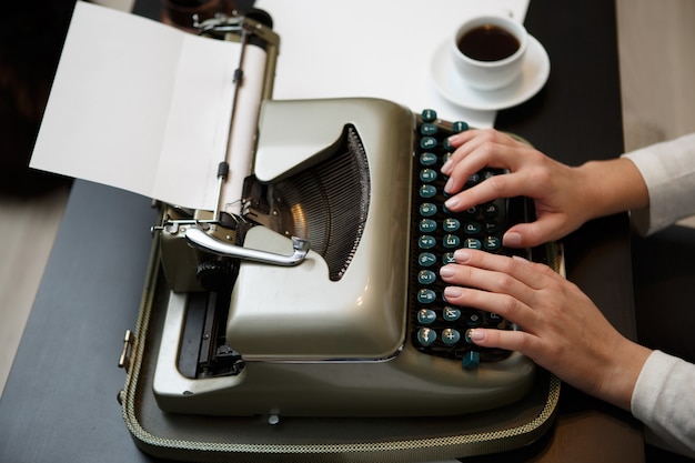 Manos escribiendo en vieja máquina de escribir cerca de la taza blanca