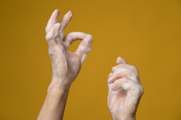 Manos en espuma jabonosa una de ellas muestra un signo de ok con los dedos