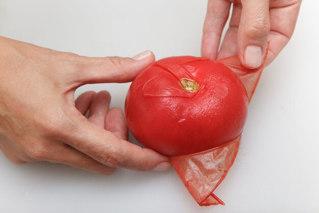 Foto las manos están quitando la cáscara del tomate rojo