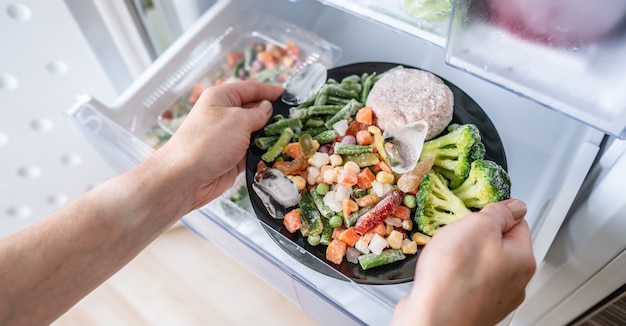 Las manos están sacando un plato de comida congelada del congelador de la nevera