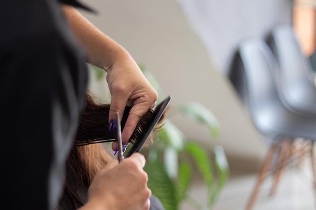 Manos de un estilista haciendo un corte de pelo con un peine y tijeras, con las uñas pintadas de azul