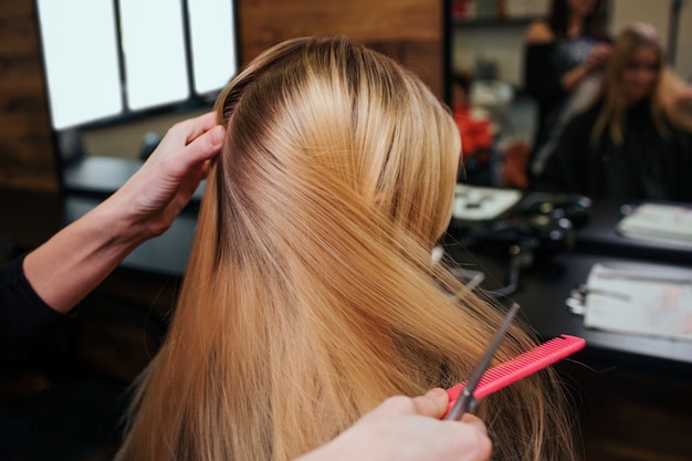 Manos de estilista peinando el cabello rubio antes de los procedimientos de cuidado del cabello en un salón de belleza