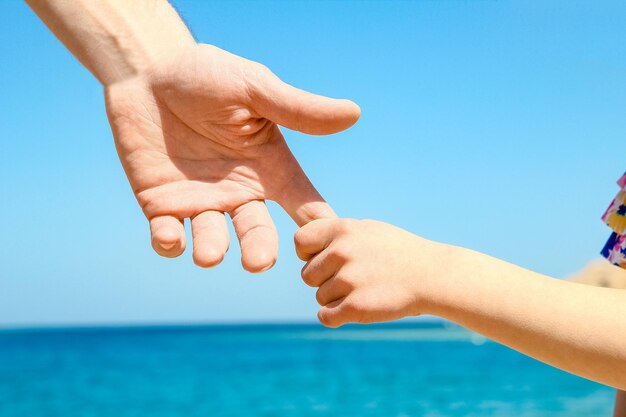 Manos con estilo de un padre y un niño en el fondo de la orilla del mar