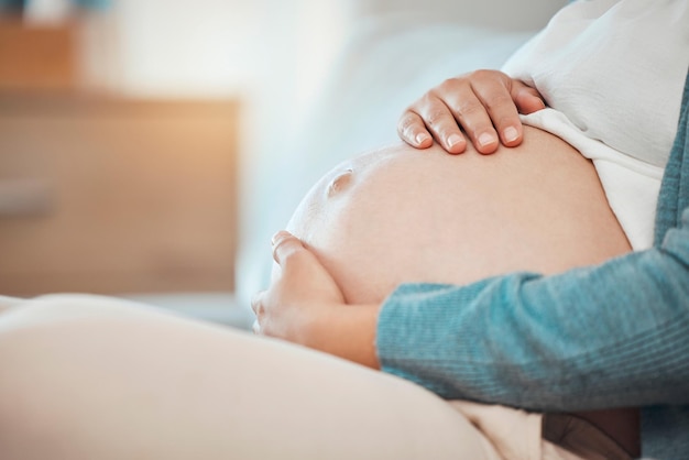 Manos en el estómago y embarazada de una mujer sentada en el dormitorio de su casa sola mientras toca su vientre Amor de madre y bebé con una madre sosteniendo su barriga mientras está en la cama para relajarse