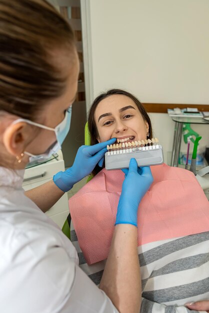 Foto manos de estomatólogo sosteniendo muestras de dientes para el tratamiento de blanqueo paciente femenina