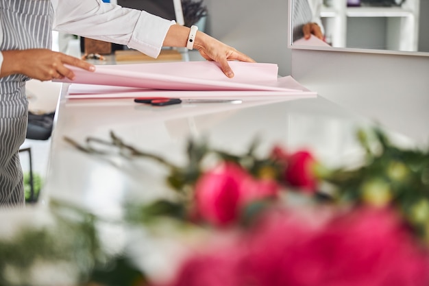 Manos expertas de un trabajador de la tienda de flores tocando el papel de regalo