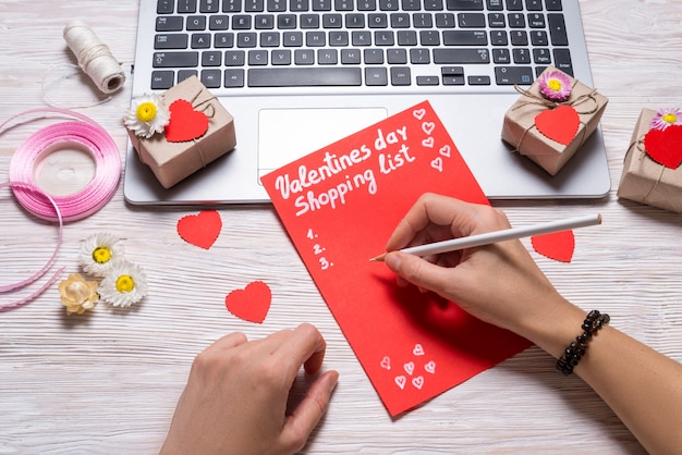 Foto manos exprimiendo la lista de compras del día de san valentín en el escritorio de madera