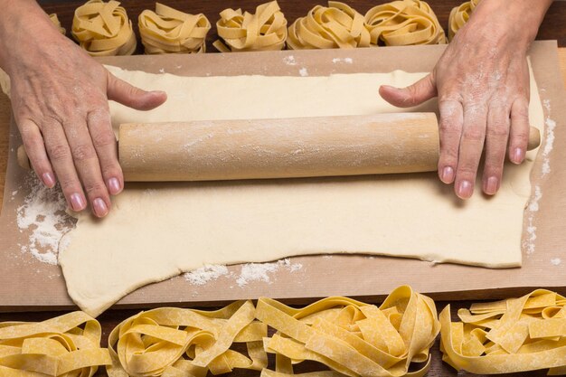 Las manos extienden la masa con un rodillo. Proceso de elaboración de la pasta para cocinar