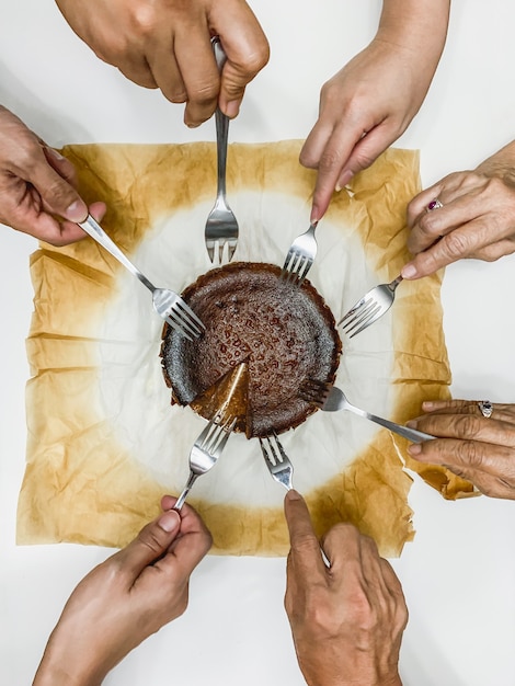 Manos de familia con tenedor comiendo pastel de queso y chocolate.