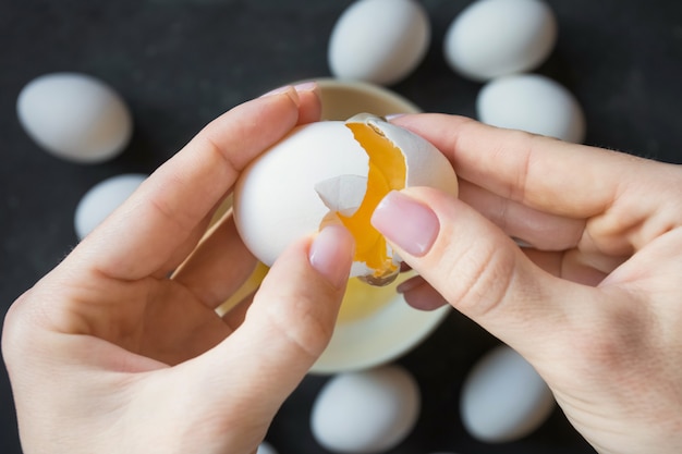 manos femeninas abren la cáscara de huevo de gallina