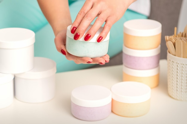 Manos femeninas abren un frasco de crema para el cuerpo blanco sobre la mesa con muchos frascos de cosméticos.