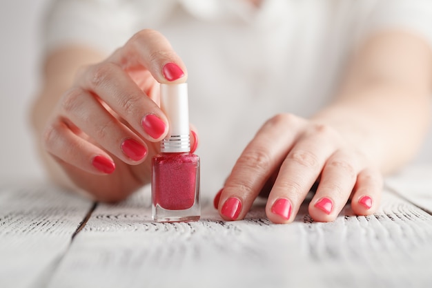 manos femeninas abriendo botella de esmalte de uñas