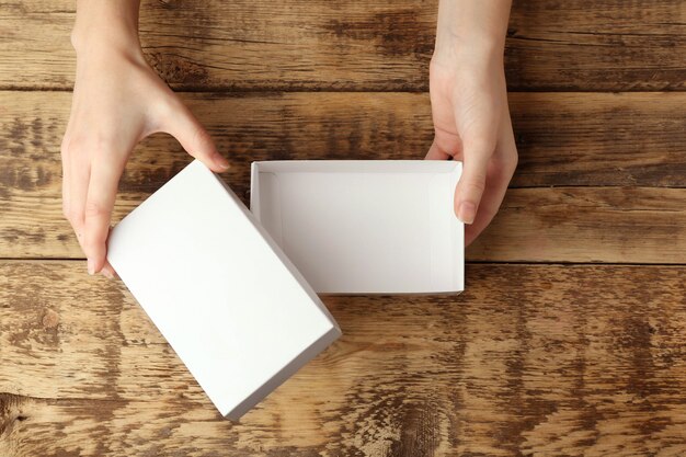 Manos femeninas abriendo caja blanca sobre fondo de madera