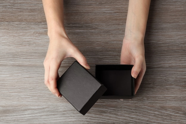 Foto manos femeninas abriendo caja negra, sobre fondo de madera