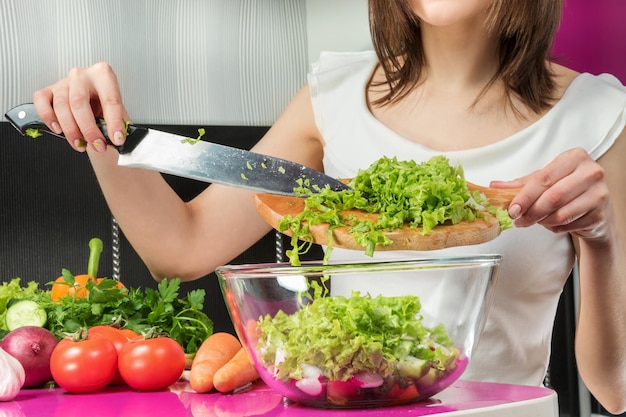 Manos femeninas agregando hojas de lechuga en un tazón con ensalada, primer plano