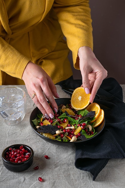 Manos femeninas agregando rodaja de naranja a la ensalada de verduras frescas, estilo de vida vegetariano