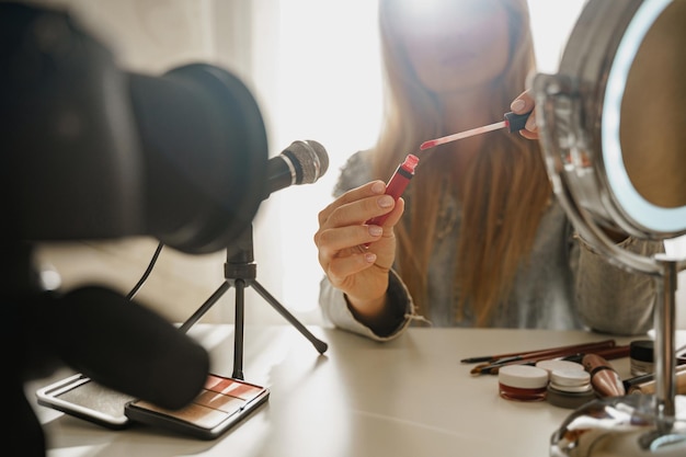 Manos femeninas con aplicador de pincel de lápiz labial Mujer bloguera de belleza haciendo una reseña en video de productos cosméticos