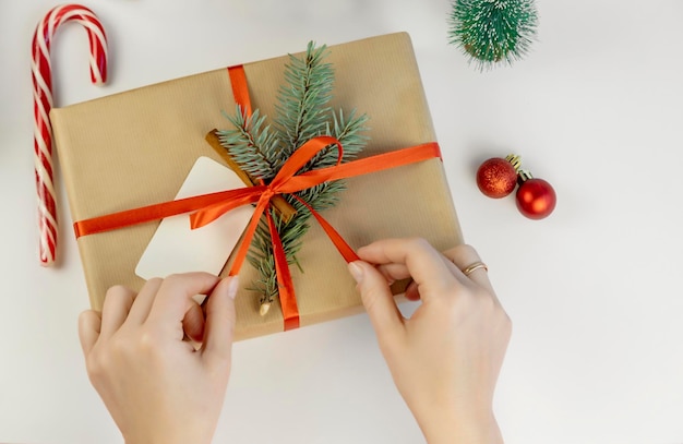 Manos femeninas atan una cinta en una caja de regalo decoraciones navideñas en un fondo blanco