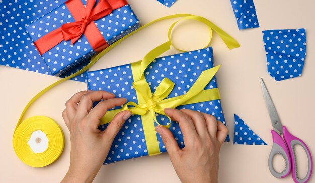 Foto manos femeninas atando un arco de seda amarillo en una caja de regalos azul preparando una vista superior sorpresa