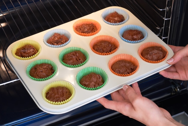 Manos femeninas con bandeja para hornear con masa de chocolate crudo en vasos de papel de colores