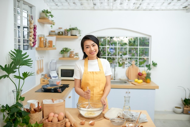 Manos femeninas batiendo huevos en un tazón, usando un batidor de huevos.