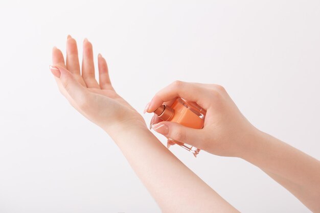 Manos femeninas con botella de perfume sobre fondo blanco.