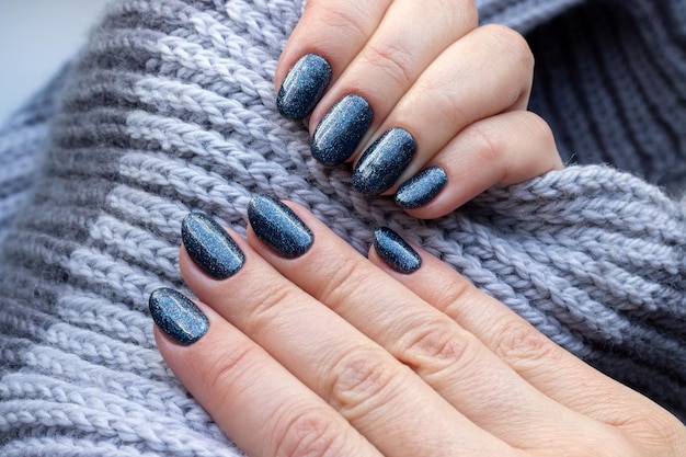 Manos femeninas con bufanda de punto gris con hermosa manicura uñas azules brillantes enfoque selectivo c...