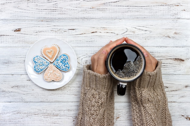 Manos femeninas con café y galletas en forma de corazón en la mesa de madera, vista superior