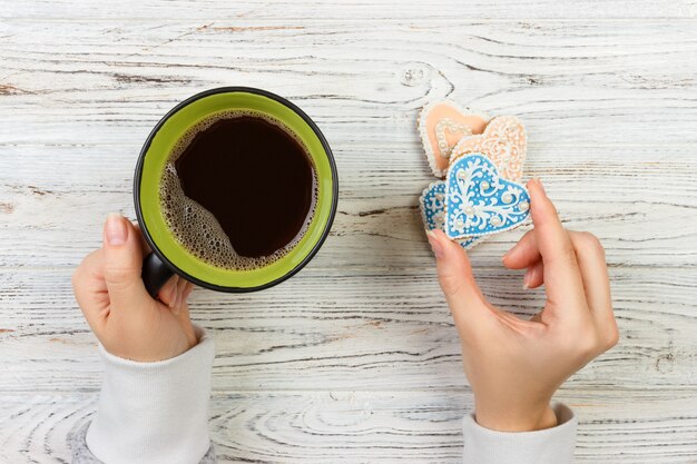 Manos femeninas con café y galletas en forma de corazón en la mesa de madera