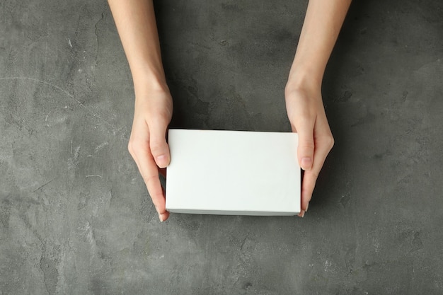 Manos femeninas con caja blanca sobre fondo de textura gris