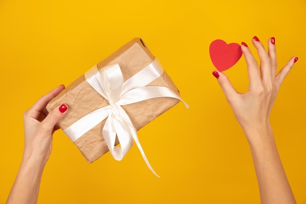 Manos femeninas con caja de regalo envuelta y corazón artificial Tiernas manos femeninas con uñas rojas