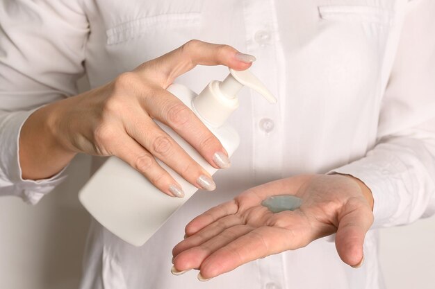 Foto las manos femeninas con una camisa blanca sostienen un dispensador de plástico blanco