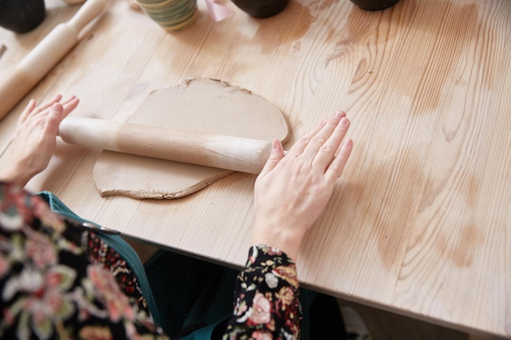 Foto las manos femeninas del ceramista extienden la arcilla sobre la mesa con un rodillo de madera.
