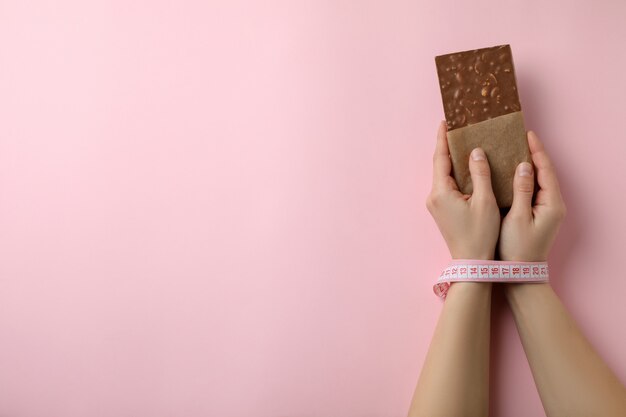 Manos femeninas con cinta métrica mantenga barra de chocolate aislada