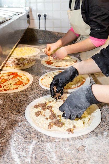 Manos femeninas cocinando en la cocina poniendo los ingredientes en la pizzaProducción y entrega de comida pizza Manos en guantes preparando pizza en restaurante italiano