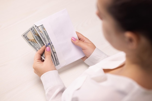 Manos femeninas comprobando billetes de un dólar en un sobre testigo sobornando a una empresaria de salario ilegal