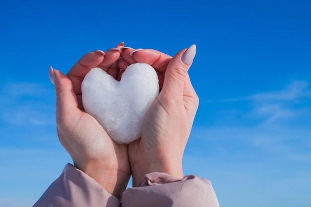 Manos femeninas con corazón blanco de nieve en día de invierno Concepto de amor