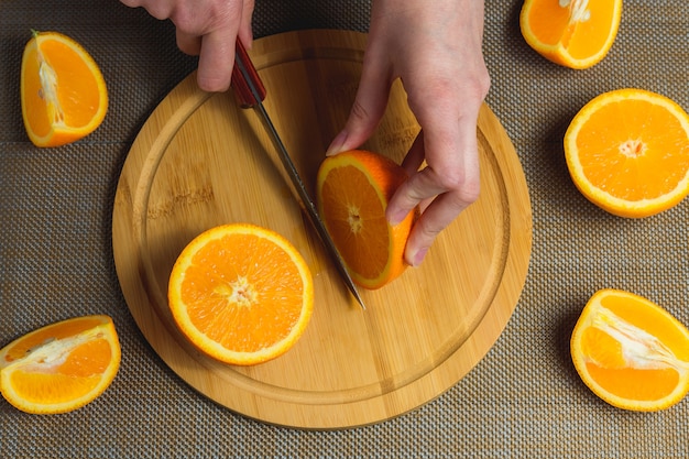 Las manos femeninas cortan la naranja con el cuchillo en la tabla de cortar de madera. Frutas Concepto saludable Vista superior.
