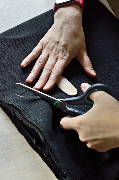 Manos femeninas cortan la tela negra con unas tijeras. de cerca.