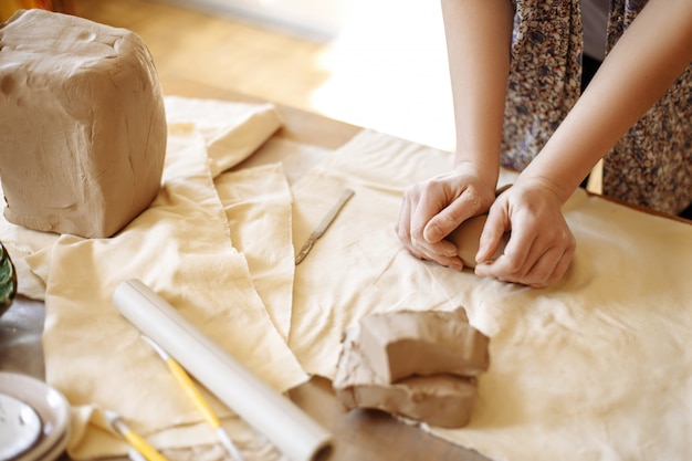 Manos femeninas cortando arcilla para crear cerámica, sobre la mesa en el taller