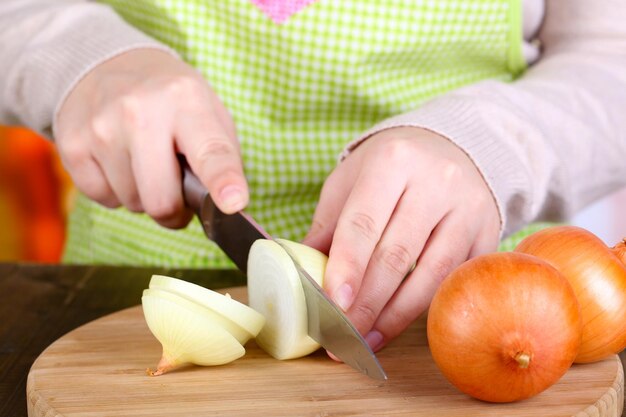 Manos femeninas cortando cebolla de bulbo en el fondo de la cocina