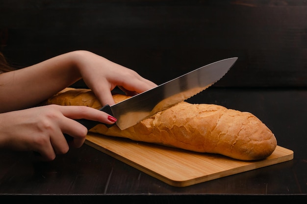manos femeninas cortando pan en una tabla de cortar sobre un fondo de madera