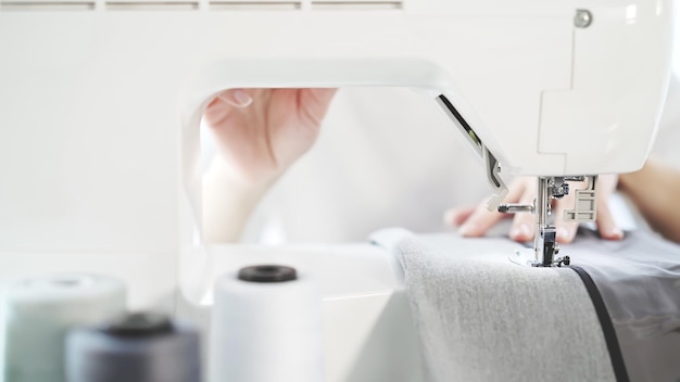 Manos femeninas cosen en un primer plano de la máquina de coser blanca