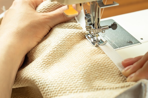 Manos femeninas cosiendo tela blanca en una máquina de coser moderna Vista de cerca del proceso de costura
