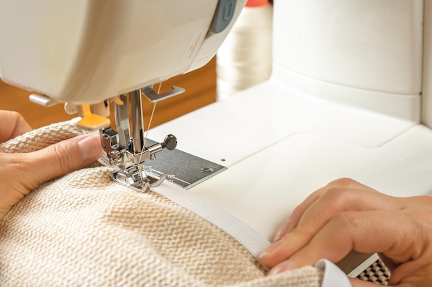 Manos femeninas cosiendo tela blanca en una máquina de coser moderna Vista de cerca del proceso de costura